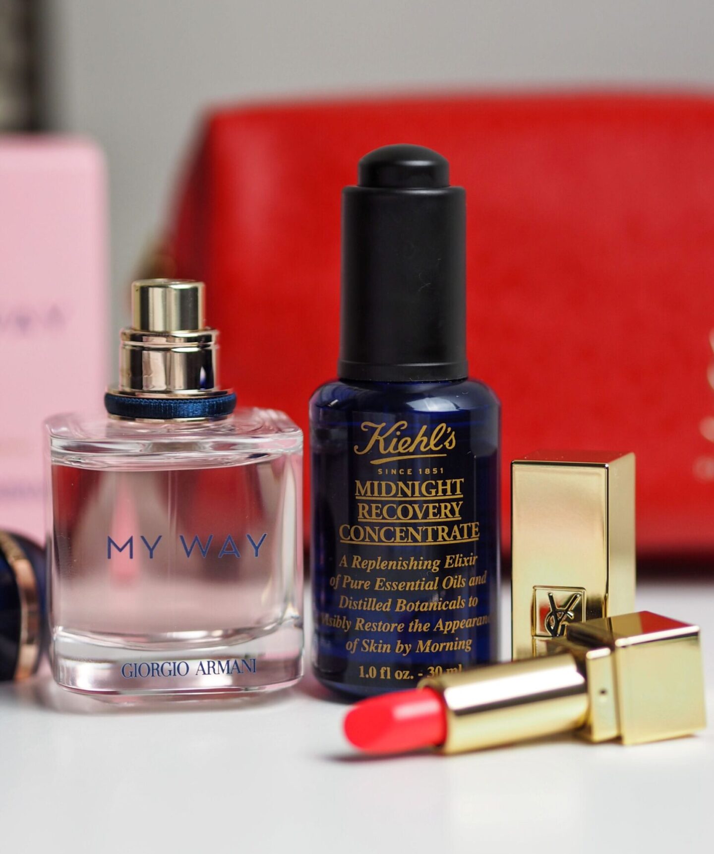 Giorgio Armani My Way perfume, Kiehl's Midnight Recovery Concentrate, and a pinky red YSL lipstick on a white table